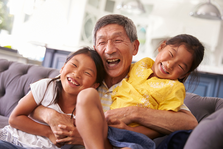 Grandfather And Granddaughters Relaxing On Sofa At Home